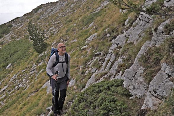 Earlier, a person is walking among grasses and low bushes, with some rocks to his right. Based on clothing, the situation looks less hostile than it is later.