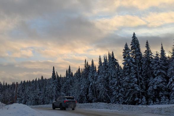 A car drives away from Le Massif at golden hour. The sky is yellow-ish and cloudy, with some blue peeking through.