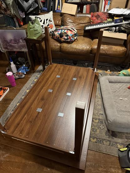 A picture of the gaming table flipped upside down which is how almost all of the construction needs to be done on it and it's very fiddly. You can see the plates that hold the bottom inside together. It's a dark walnut colored wood but it's made out of pressboard.