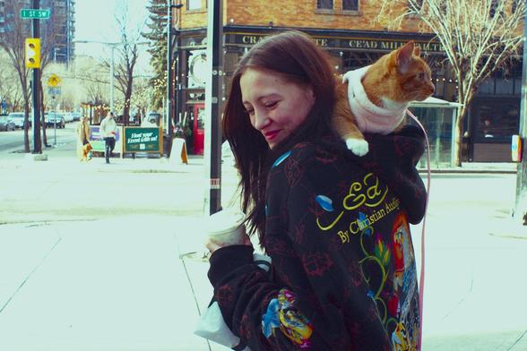 Woman with colourful jacket and cat crawling on her shoulder.