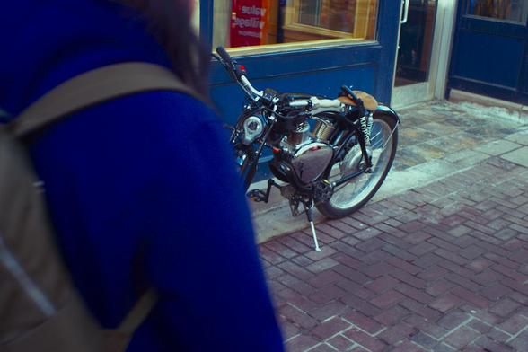 Some kind of faux motorcycle bicycle. Person close in foreground with blue coat partially blocking.