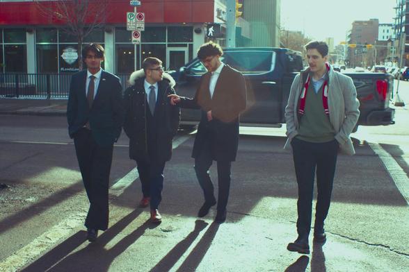 Four men walk towards camera in nice suits. Long shadows.