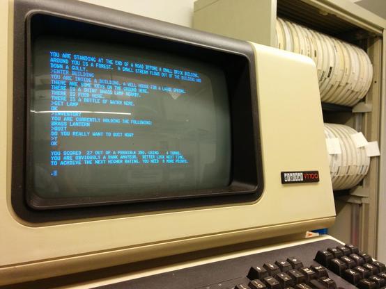 terminal with all caps adventure game displayed on it.  a rack of tapes hangs in the background