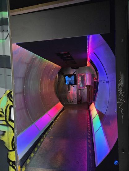 A spaceship esque hallway at c-base Berlin with rounded metal walls and rainbow neon lights.