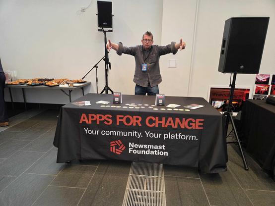Ben points to a table decorated with Newsmast Foundation branding.