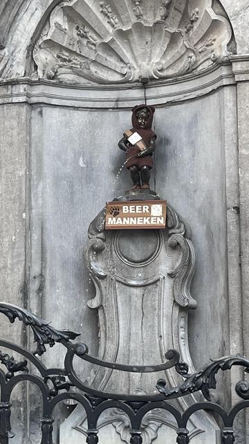 Mannaken Pis in a brown bear onesie. His sash has a bear icon and the sign below him reads: BEER MANNEKEN.