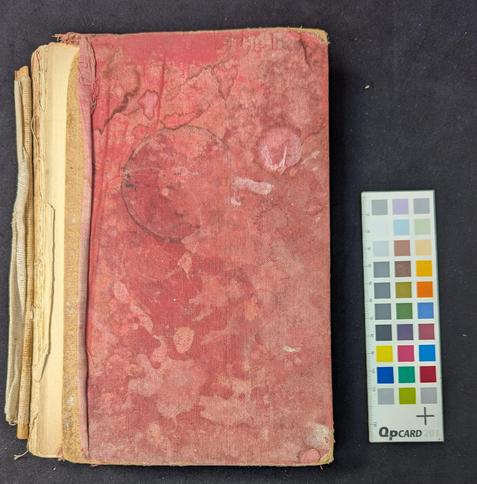 Front cover of a red cloth covered book showing water stains, tea cup stain, missing spine.