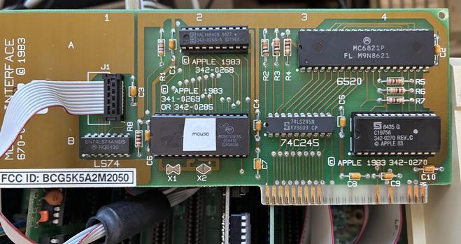 An Apple ii mouse card - basically a small rectangular board with six ICs on it, and a gold plated edge connector to the bottom right. 

To the far right is a soldered in IDC cable, which goes off to the mouse port. 

There is a wide 28 pin IC, which is labelled as a MC68705P3S, which is the EPROM version of the 6805 (usually that uses a factory mask Rom).

There’s a helpful label of “mouse” covering the EPROM window