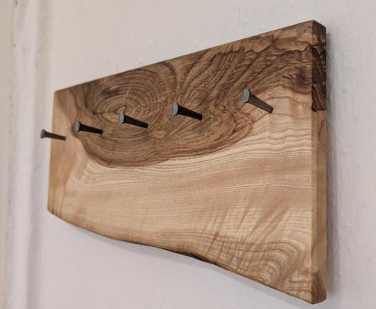 The key holder consists of a simple board screwed on a wall with five iron nails. The board has three straight sides, and the forth, downward-facing side is left wavy. The top part also shows the chocolatey-brown heartwood while the lower part consists of the light outer wood of the ash log, with some curly grain patterns. The thick iron nails have a pronounced head, and are tilting slightly upward so that the keys cannot slide off.