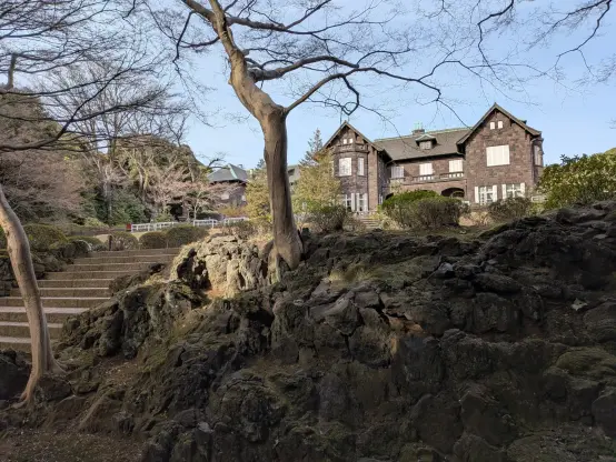 Photo: In the Kyu-Furukawa Gardens, Tokyo, a ground elevation with several mossy rocks and trees. On the left side, several stone steps. Beyond the elevation, in the back, a western-style mansion.