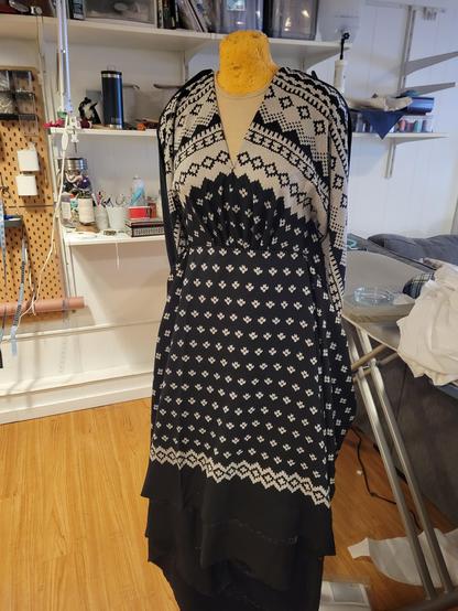 Yards of black wool fabric pinned up on a dress form. The print is a faux fat knit design , with a heavy white band in a design similar to what you would see on a knit sweater. The fabric is pinned to form a deep v neckline, and the pattern forms an arch  as it gets to the waistband. 

The print at the hem is a much simpler and narrow. While only pinned up, it is a pencil skirt in shape with a wide, loose blouse on top.