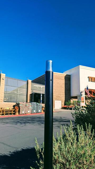 Photograph of a tall black pole in a parking lot which appears to have the top portion of it uninstalled revealing only a bare steel inner sleeve and the top has been unbolted and removed.