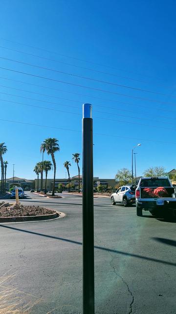 Photograph of a tall black pole in a parking lot which appears to have the top portion of it uninstalled revealing only a bare steel inner sleeve and the top has been unbolted and removed.