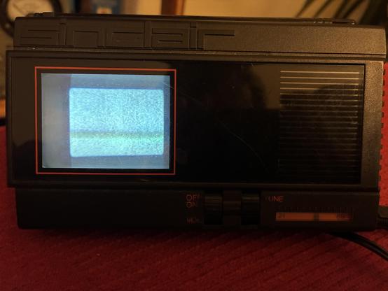 A small black portable telvision, with Sinclair branding. The flat CRT is powered up and showing static on the screen
