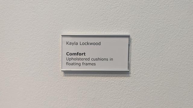 the placard on the wall of this gallery identifies the art piece as one by a Kayla Lockwood entitled "Comfort"