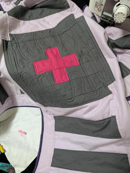 A hot pink cross set in grey. The grey has a wavy squirmy wiggly line wandering around it, kind if like a worm.
