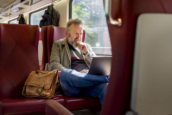 Een man zit in de trein en kijkt op zijn laptop.