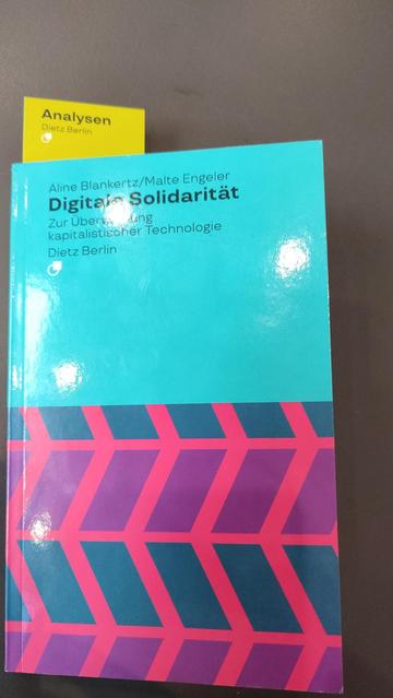 Photo of the cover of the book 'Digitale Solidarität' by Aline Blankertz and Malte Engeler. A blueish background on the top halve with text in black, is complemented with skewed rectangles in purple and dark blue on a pinkish red background.
