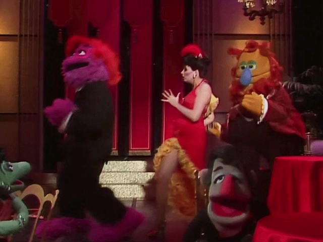 GIF of Liza Minnelli as a showgirl dancing at the Copacabana with two full-body Muppets