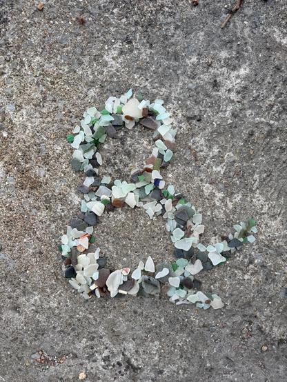An ampersand made of beach glass, on what looks like maybe a concrete slab.