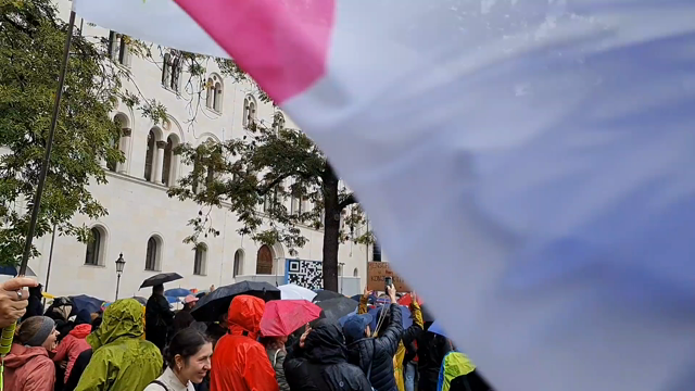 Kurzer Videoausschnitt von der Demo. Menschen mit Regenschirmen wippen zur Musik mit. Im Vordergrund wird eine große AfD-Verbot Jetzt Fahne geschwenkt.
