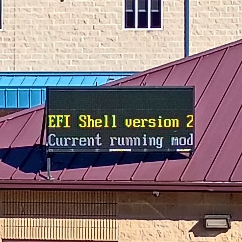 a large billboard on a beige building's red roof, showing stock boot EFI text instead of any graphics. the billboard reads "EFI Shell version 2-" and "Current running mod-", cut off due to the internally rendered size of the display