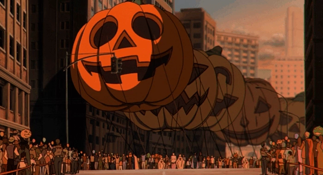 Clip from an anime with a street parade where giant balloon pumpkin jack-o-lanterns are being led down a city street, with large crowds. All the balloons are carved pumpkins.