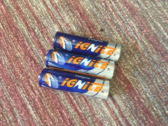 Three AA batteries sitting on my carpet. They have a blue and silver color scheme with orange accents. They are "IGNITE" branded.
