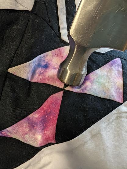 A hammer head resting on a quikt, near the intersection of 6 seams that meet in the center of three triangles.