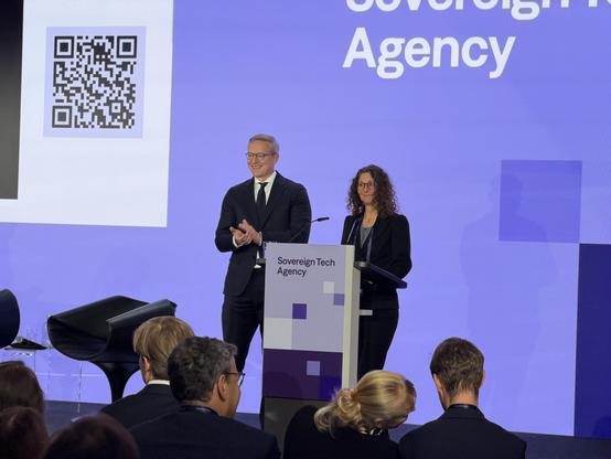 Foto von Luisa von Beust, wie sie neben Digitalminister Karsten Wildberger auf der Bühne steht. Auf dem Podium steht Sovereign Tech Agency.