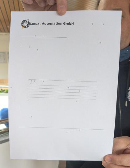 Jemand hält ein Blatt Papier vor die Kamera. Der Inhalt sieht aus wie ein Dokument, oben ist das Logo der "Linux Automation GmbH" zu erkennen, aber der Rest des Dokuments besteht nur aus einer Sammlung von großen und kleinen Buchstaben S mit vielen weißen Lücken dazwischen und ein paar horizontalen Linien.