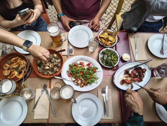 A long table with a few shared platters of food in the middle. 
There is a plate of cooked prawns; a plate of garlic clams; a colourful salad with sliced octopus, rocket, red and yellow cherry tomatoes; a bowl of crispy fried potato skins with aioli; a plate of grilled chorizo; and a bowl of charred green peppers