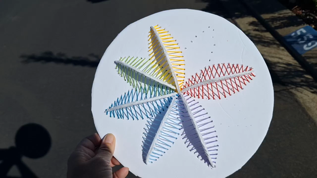 A circle of white foam board has colorful stitching between it and small pieces of white board standing perpendicular against it.