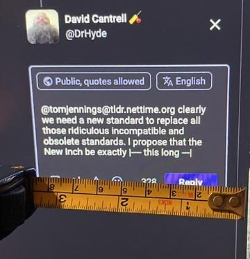 Photograph of me measuring the New Inch on my screen, using a tape measure, to see how it compares to one of the many obsolete previous standards