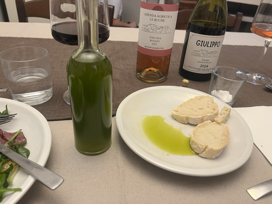 Spisebord med tallerkener og vinglas. Midtfor en lille glasflaske med græsgrøn olivenolie ved siden af en lille tallerken med olie og brødskiver