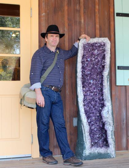Mann steht neben einer zirka 160cm hohen Druse mit violettem Mineral