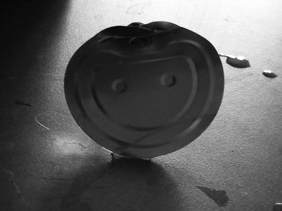 The lid of a tin can is lying on a worktop, and the indentations on the back of it resemble a smiley or happy face. The picture is in black and white.