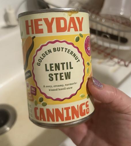 A hand holding a colorful can which says "Heyday Canning" and "golden butternut lentil stew, a cozy, creamy turmeric-kissed lentil stew"