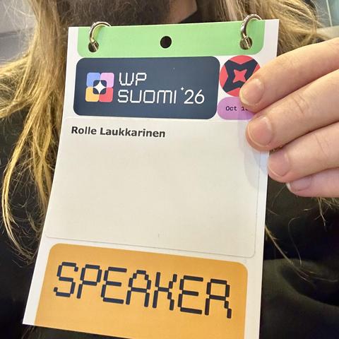 Conference badge with "SPEAKER" text, held by a person's hand, for the WP Suomi 26 event, featuring a name "Rolle Laukkarinen".