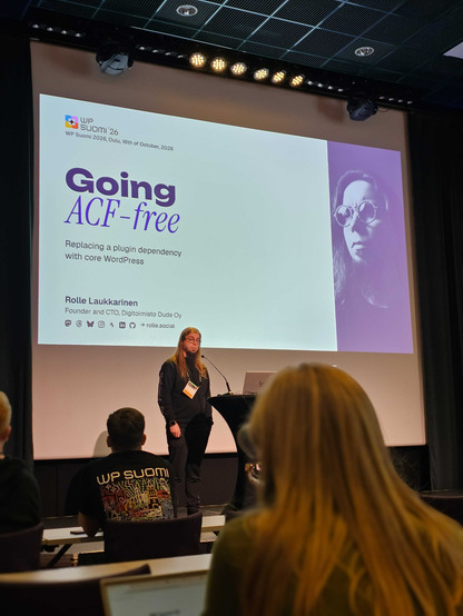 Rolle giving a presentation on stage at a WordPress Finland (WP Suomi) conference, with a large screen displaying the title "Going ACF-free".
