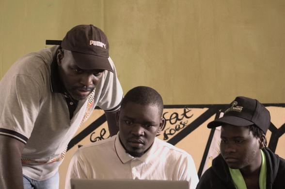 Dilman Dila standing next to a couple students he's mentoring as they look at a laptop screen.