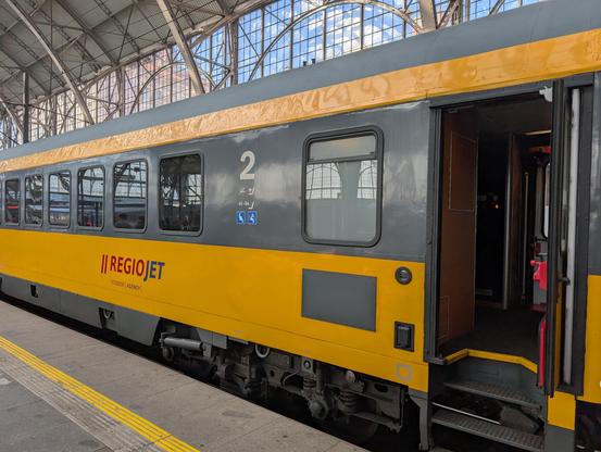 Yellow RegioJet train on the platform: traditional carriages with 3 steps to enter.