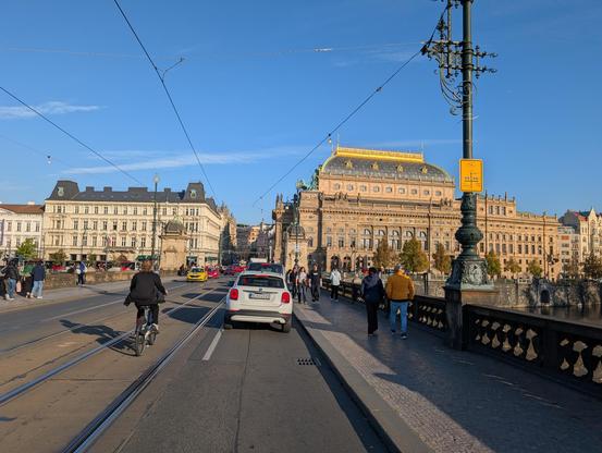 Narrow lane on a bridge filled with a traffic jam, and tram tracks next to it that a cyclist rolls into. There is also a small sign for cycling directions on a lamp post, barely readable from this distance.