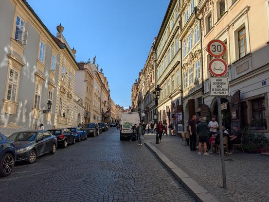 Paved 30 km/h zone in a touristic area, with a sign forbidding electric scooters. Despite parked cars taking a lot of space on both sides.