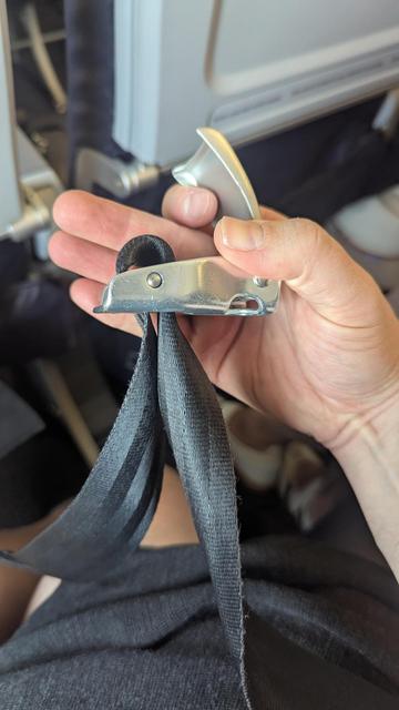 an airplane seatbelt buckle seen with the nylon belt partially twisted around and being fed through the buckle