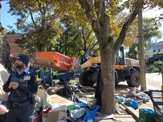Oct 16, 2025: Security guard watching protestors, as The Claw tramples and rips away peoples housing and possessions.