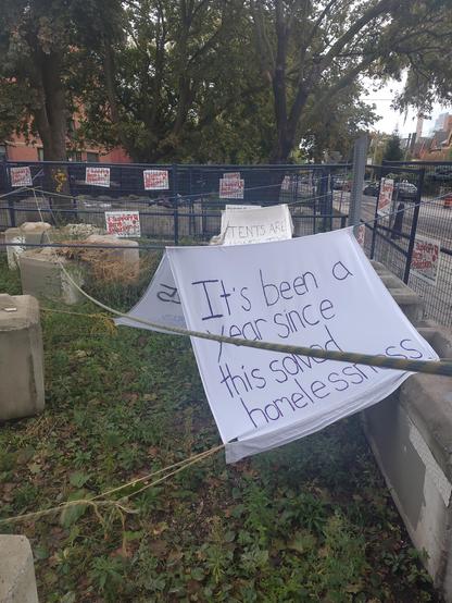 Inside the fenced-off churchyard, a hand painted sign: "It's been a year since this solved homelessness".

Smaller signs hanging on the fences say " I support harm reduction"