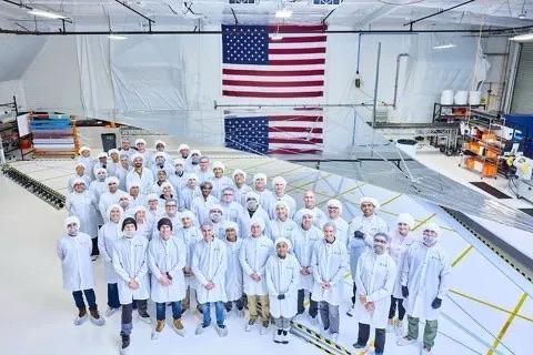 Reflect orbital employees wearing white gowns in some engineering facility with an American flag in the background