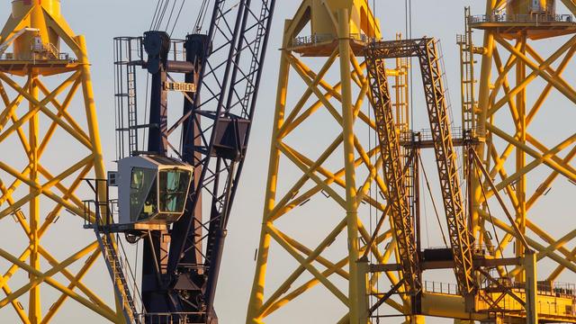 A crane cabin and part of its dark grey structure. Behind it is a little of angled yellow steel tubing, forming parts of some enormous tapering towers. They’re jacket foundations, soon to be shipped off and submerged under the North Sea to support wind turbines.