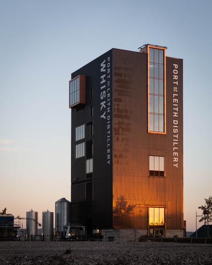 A shiny black metal-clad tower sits on the leith dockside. It’s the Port Of Leith distillery, and its cladding reflects the golden light of the sunrise, behind us.